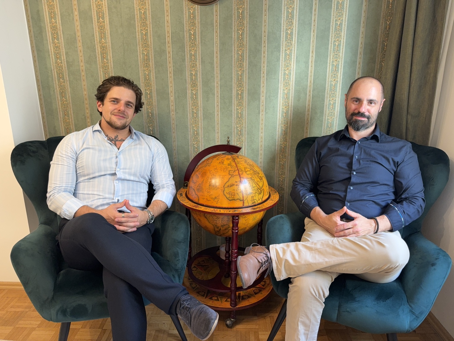 Matei Buliga und Harald Ottawa sitzen in zwei grünen Sesseln neben einem Globus.